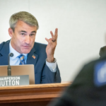 Chairperson Rob Hutton with his hands up, sitting at a desk