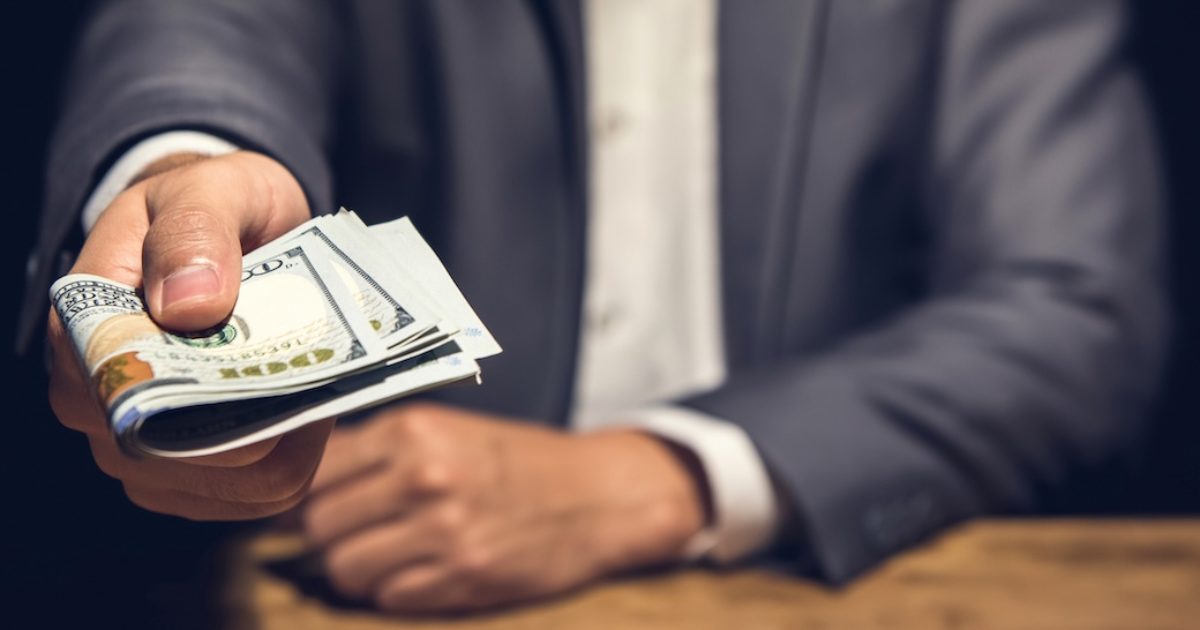 Rich businessman holding and giving US dollar money in dark private room for the invesment - bribery and corruption concept, panoramic banner