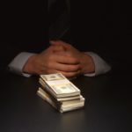 Businessman sits near a heap money on a table