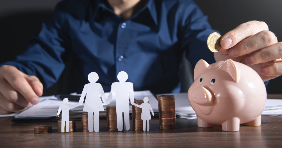 person at a desk putting a coin into a piggy bank and paper cut out of a family