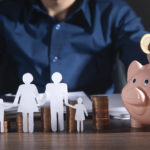 person at a desk putting a coin into a piggy bank and paper cut out of a family