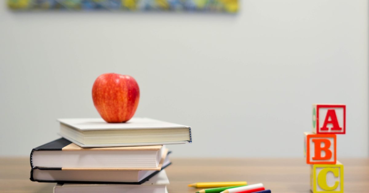 apple, school books, ABC blocks, and colored pencils on a desk