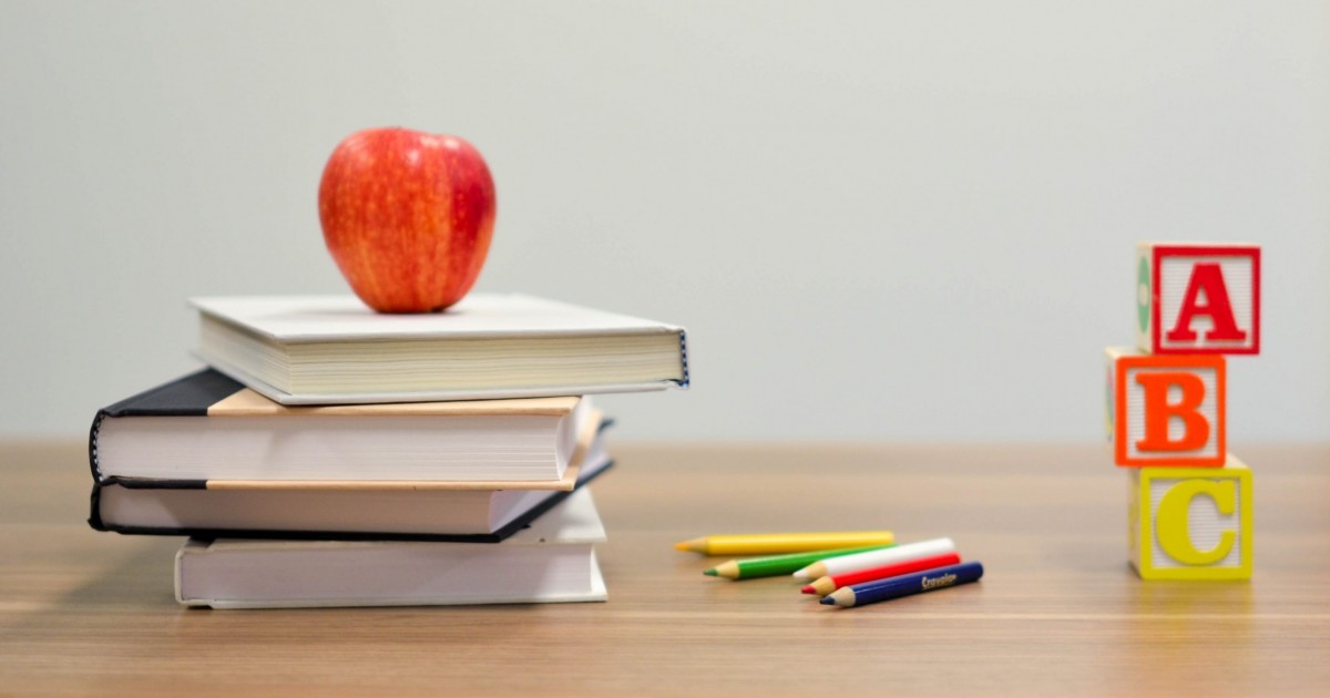 apple, school books, ABC blocks, and colored pencils on a desk