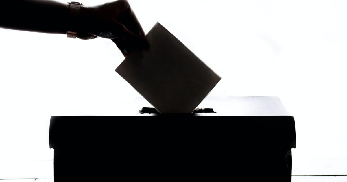 silhouette of a voter voting by putting their ballot in the a ballot box