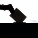 silhouette of a voter voting by putting their ballot in the a ballot box
